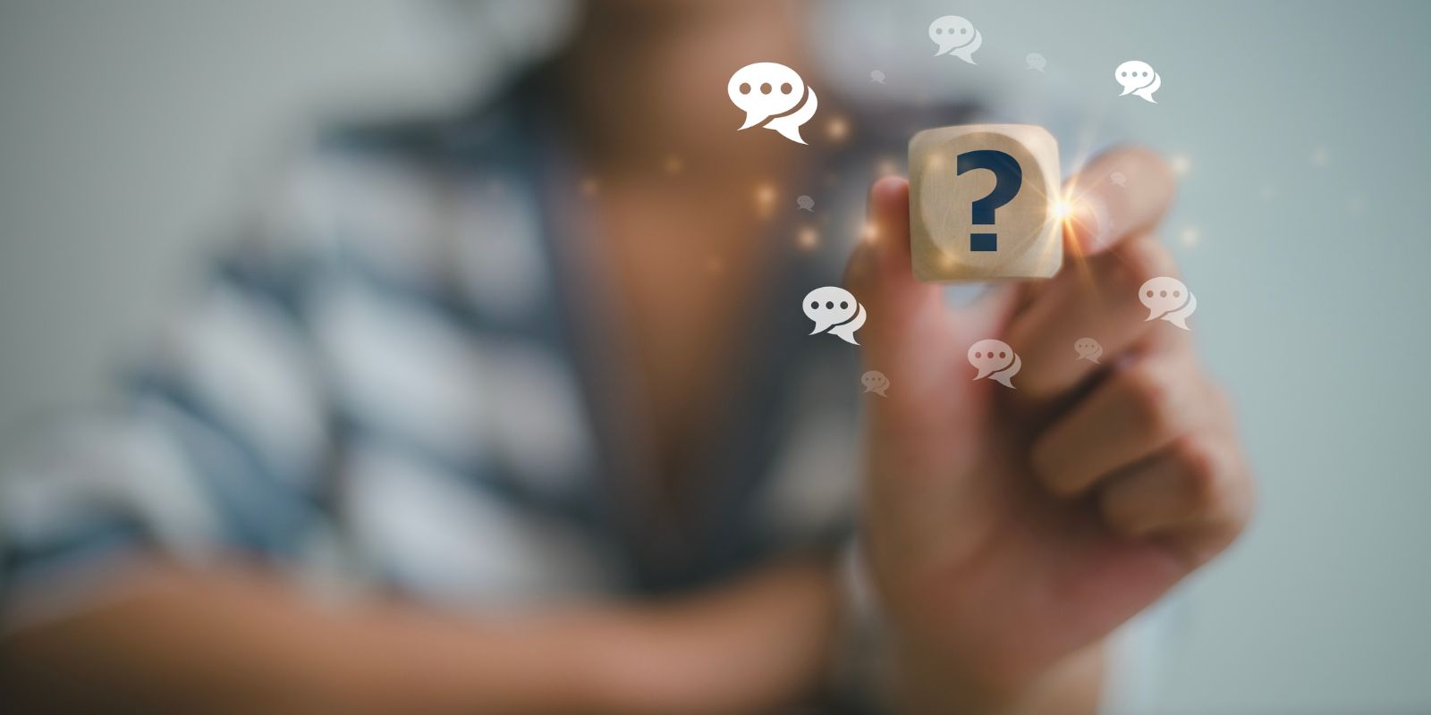 Hands reach toward a wooden cube with a blue question mark, surrounded by floating chat bubbles, portraying inquiry and dialogue.